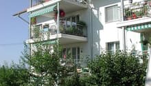 3 story white building, multiple balconies, green plants, shrubs