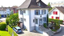 2 story house, white exterior, brown roof, blue windows, grey door, blue garage door, paved driveway, garden, lawn, hedge, mailbox, stairs, blue car parked