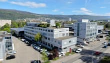 Multi-story office building with parking lot, surrounded by hills and mountains in the background