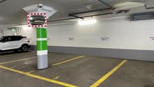 underground parking area with white walls, yellow and gray parking lines, a central pillar with a camera, a car parked