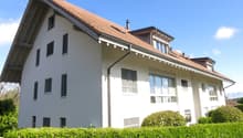 White house with red roof, multiple windows, hedges in front, chimneys
