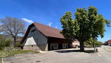 Warehouse with brown roof, concrete base, parking lot in front, trees on both sides