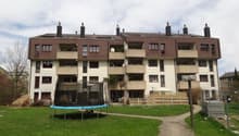 Apartment building with multiple floors, balconies, and a garden in front.