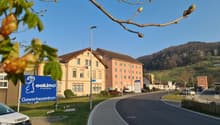 commercial building, large windows, brown roof, blue sign, grassy area, street light, parked car, mountains in the distance