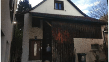 2 story house, white walls, brown roof, wooden door, steps leading to the entrance, trash bin, plants