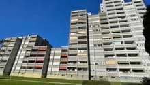 high rise apartment building, multiple floors, concrete exterior, red awnings, balconies, windows, greenery in front
