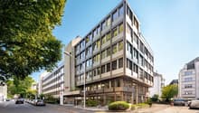 Modern office building with glass facade, multiple floors, and a corner entrance.