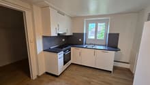 Spacious kitchen with white cabinets, black countertops, stainless steel appliances, and hardwood flooring. The kitchen has an L-shaped layout with a window providing natural light.