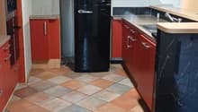 Modern kitchen with tiled floor, black refrigerator, red cabinets, white walls, a sink with faucet, a gas stove, and a fan on the ceiling