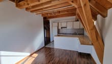 Open kitchen with wooden beams, white cabinets, wooden countertop, white walls, wooden floor