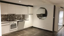 modern kitchen with white cabinets, black tiled backsplash, round mirror, dishwasher, oven, sink, tiled floor