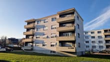 5-story apartment building, concrete balconies, flat roof, multiple windows, outdoor parking area