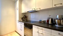Modern kitchen with white cabinets, black countertop, built-in oven and stovetop, dishwasher, and various kitchen appliances and utensils
