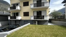 3 story building, yellow and gray exterior, multiple balconies, cars parked in front