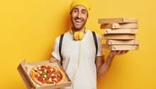 Man holding pizza boxes, smiling, wearing yellow headphones and a yellow hat