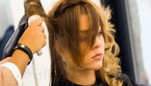 A woman with long blonde hair is getting her hair dried by a hair stylist using a hair dryer.