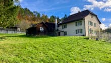 2 story house, brown roof, green shutters, wooden barn, large grassy field, trees in the background