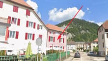 A street view of a building with red shutters and a green fence, with a mountain in the background.