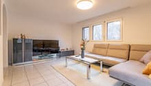 white tiles, beige sofa, glass coffee table, flat screen TV, cabinet, flowers, round lamp