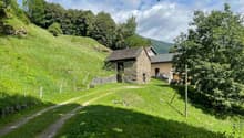 Small stone house on a slope with a balcony, located in a green landscape