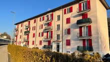 4 story apartment building, beige, red shutters, multiple balconies, hedges in front