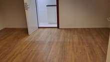 Empty room with open door to a smaller room with bathroom, wooden floor, white walls