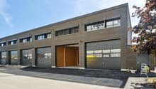 Industrial building with multiple garages, gray exterior, windows, and an open garage door.