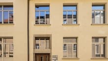 Four story building, double doors, many windows, parking space, gray color, brick facade