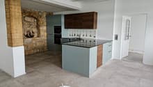 kitchen island, countertop, stone wall, cabinets, built-in oven, sink, faucet, large open room, white flooring