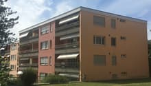 5 story apartment building, beige and red facade, multiple balconies, fenced garden in front