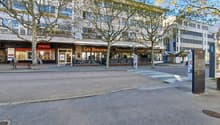 A building with many windows, a restaurant named Les Brasseur, a bench, and trees in front.