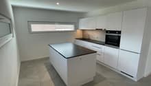 Modern kitchen with island, white cabinets, black countertops, built-in oven and microwave, sink with faucet, and tiled flooring.