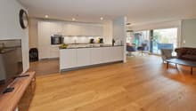 Open plan kitchen and living room, wooden floor, white cabinets, large windows, dining table, couch, TV