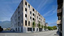 Modern apartment building with multiple floors, concrete and glass exterior, multiple windows, and a flat roof.