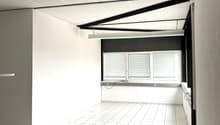 Empty office room with white tiles, modern ceiling with lighting, white walls, window with blinds, and white cabinet in the corner