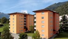 Two orange apartment buildings with multiple windows and balconies, surrounded by trees and a parking lot.