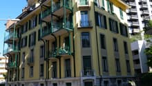 5 story building, yellow exterior, green balconies, multiple windows, stone base