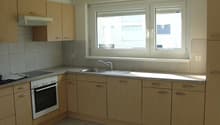 Spacious kitchen with light wood cabinets, granite countertops, stainless steel appliances including a dishwasher, and large windows providing natural light.