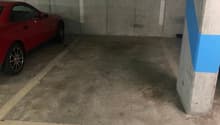 concrete floor, two doors on the wall with numbers, red car parked, empty parking area
