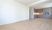 Empty room with wooden floor, white walls, kitchen with cabinets, microwave, and drawers, power outlets on the wall.