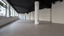 Empty room, white walls, black ceiling, gray tile floor, large windows, pillars