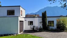 modern style house, white walls, brown roof, garage, large windows, surrounded by plants and trees, with a mountain view