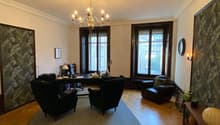 Wooden floor, wooden desk, three black chairs, one armchair, lamps, large windows, chandelier