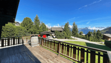 wooden deck, wooden railing, barrel, green grass, trees, mountains