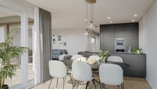Spacious open-concept living area with a dining table, gray upholstered chairs, and a modern kitchen with dark cabinets and appliances. Large windows and sliding glass doors provide access to a balcony or terrace. The room is decorated with artwork and po
