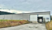 Large industrial building with one main entrance, a large opening on the side, and a smaller building next to it. Parking lot in front.