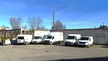 Several white vans parked in a lot with an electric pole and power cables.