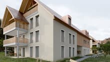 3-story apartment building with a modern, mixed-material design featuring wooden accents and balconies. The building has a grassy area with benches and toys, suggesting it may be a family-oriented residential complex.