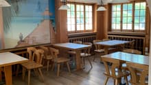 Cozy dining room with wooden tables and chairs, large windows, and a mural depicting a beach scene on the wall.