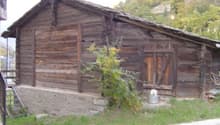 Old wooden cabin with a slanted roof, wooden walls, and a garage or storage area attached to the side.